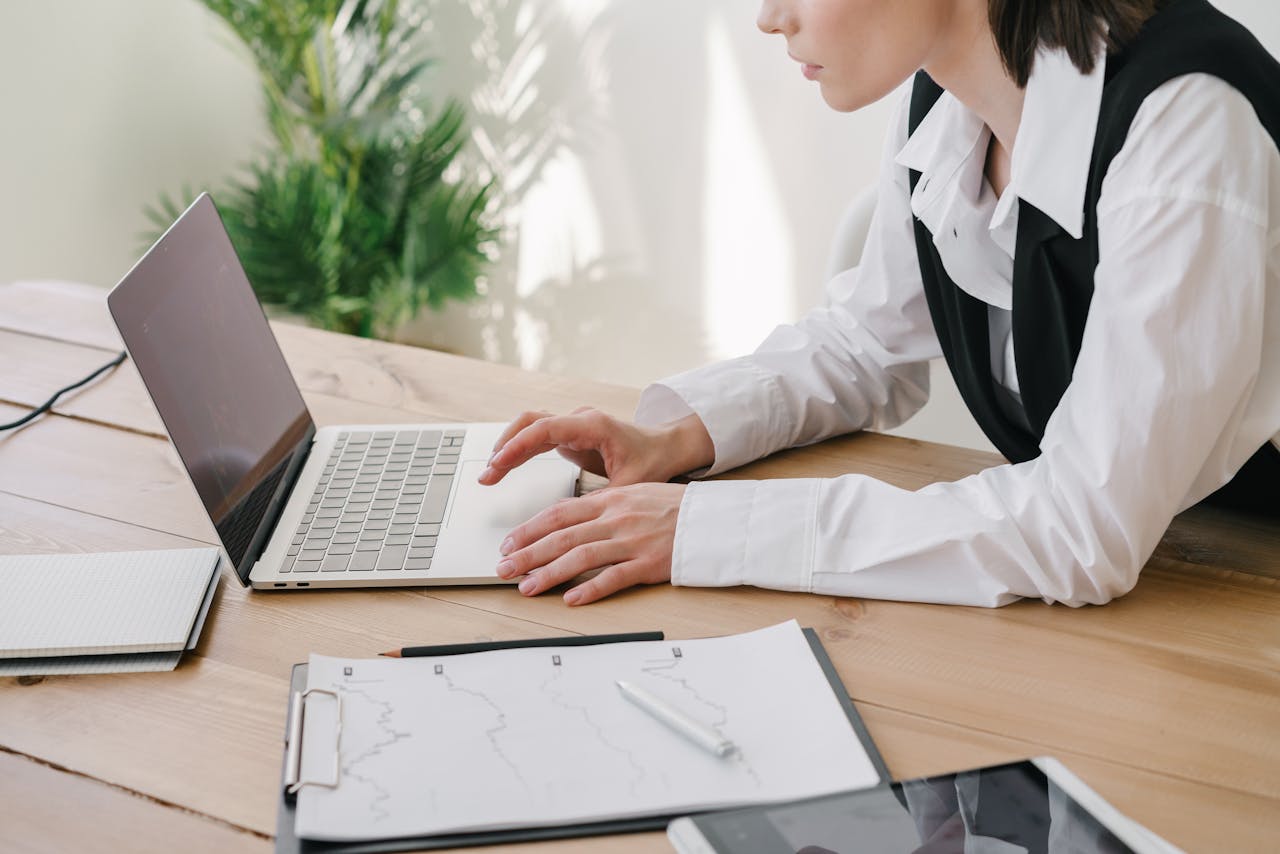 Professional woman using laptop at a wooden desk with office supplies.
